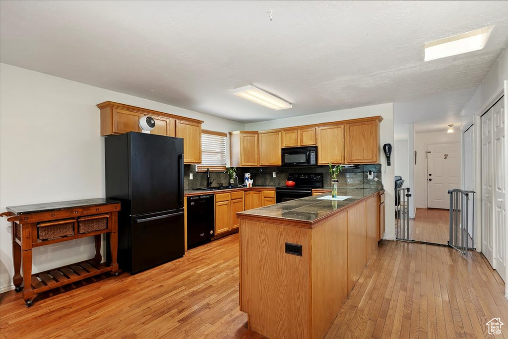 Kitchen featuring black appliances, a peninsula, light wood-style flooring, tasteful backsplash, and tile counters