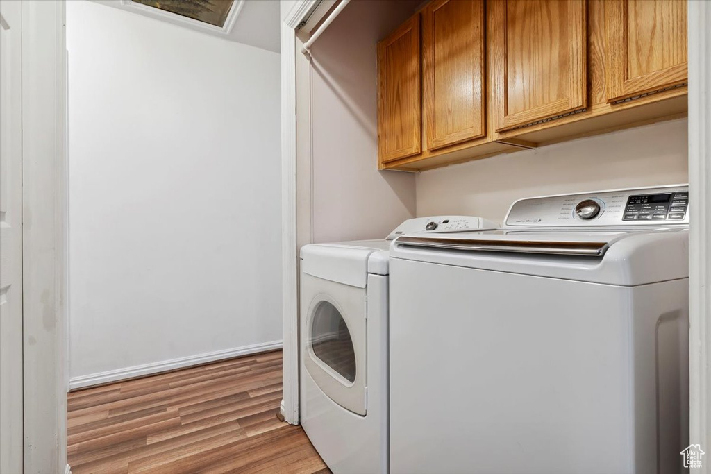 Washroom featuring independent washer and dryer, light wood-style flooring, and cabinet space