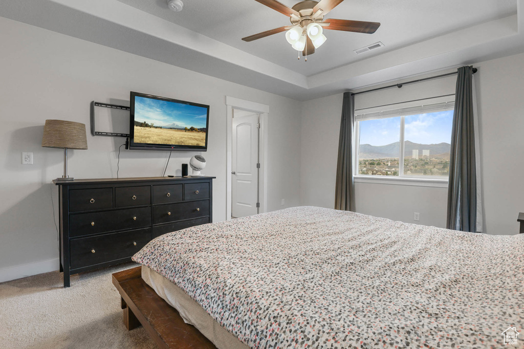 Carpeted bedroom with a tray ceiling and a ceiling fan