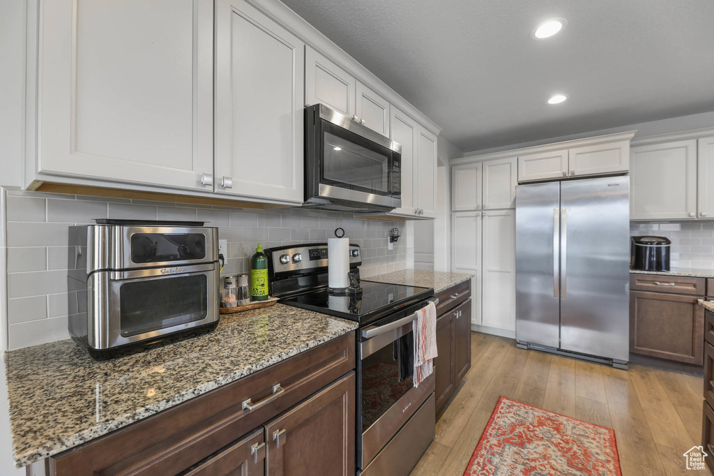 Kitchen with appliances with stainless steel finishes, tasteful backsplash, white cabinetry, light wood-type flooring, and light stone countertops