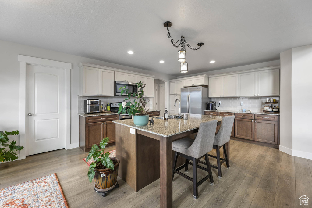 Kitchen featuring appliances with stainless steel finishes, light wood finished floors, recessed lighting, tasteful backsplash, and light stone countertops