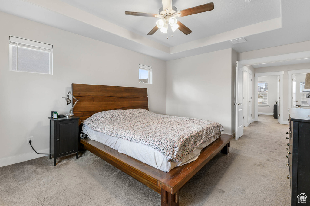 Bedroom featuring light colored carpet, a raised ceiling, and a ceiling fan