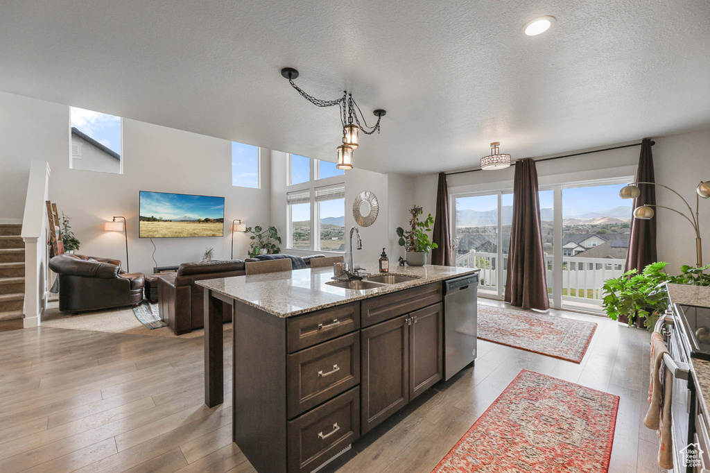 Kitchen with appliances with stainless steel finishes, dark brown cabinets, a textured ceiling, hanging light fixtures, and light stone countertops