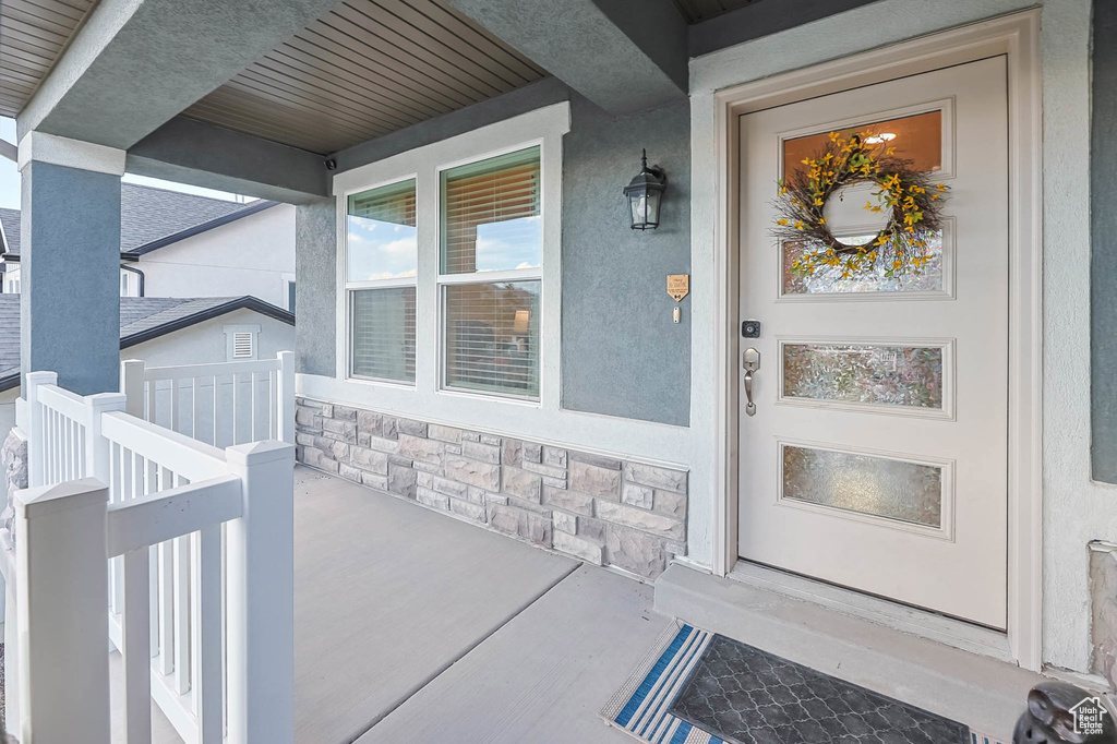 View of exterior entry with covered porch, stone siding, and stucco siding