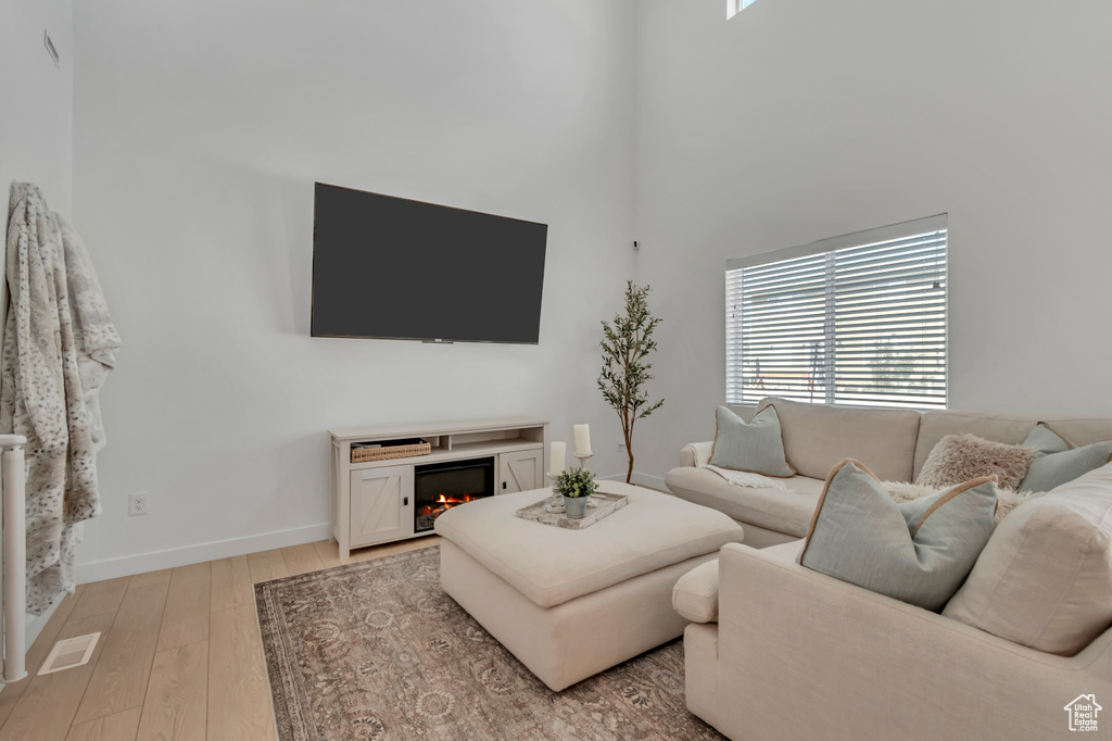 Living area featuring a lit fireplace, light wood-type flooring, and a high ceiling