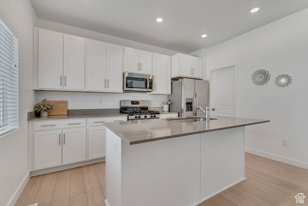 Kitchen featuring appliances with stainless steel finishes, a center island with sink, light wood-style flooring, white cabinetry, and recessed lighting