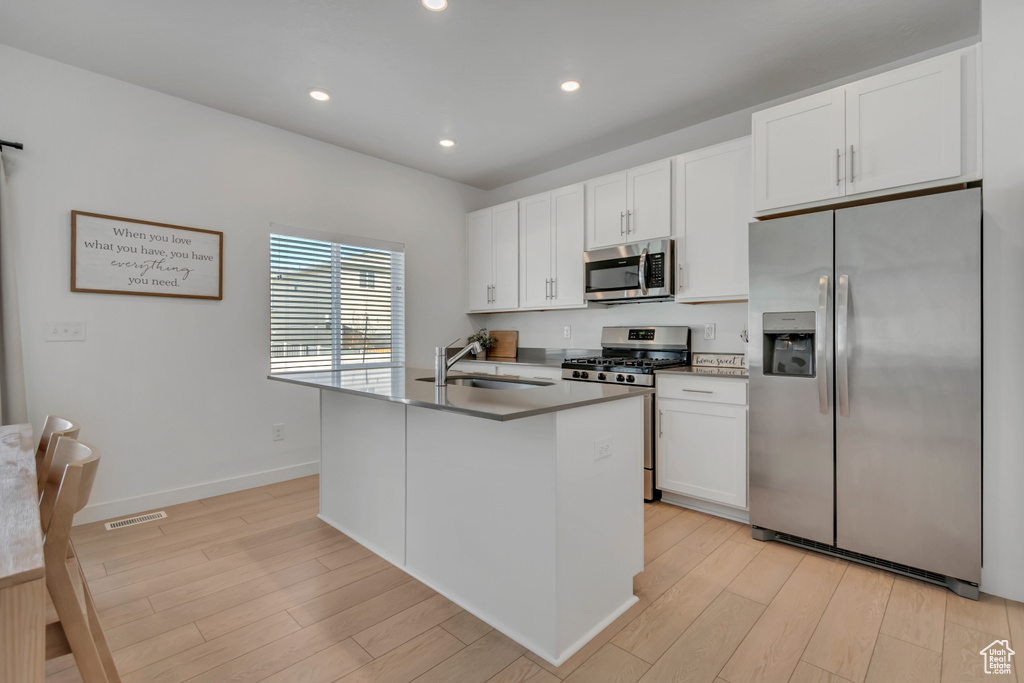 Kitchen with appliances with stainless steel finishes, light wood-style flooring, white cabinets, a kitchen island with sink, and recessed lighting