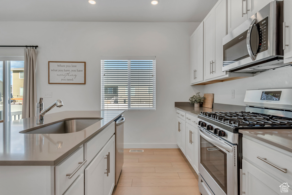 Kitchen with stainless steel appliances, plenty of natural light, recessed lighting, light wood-style floors, and white cabinets