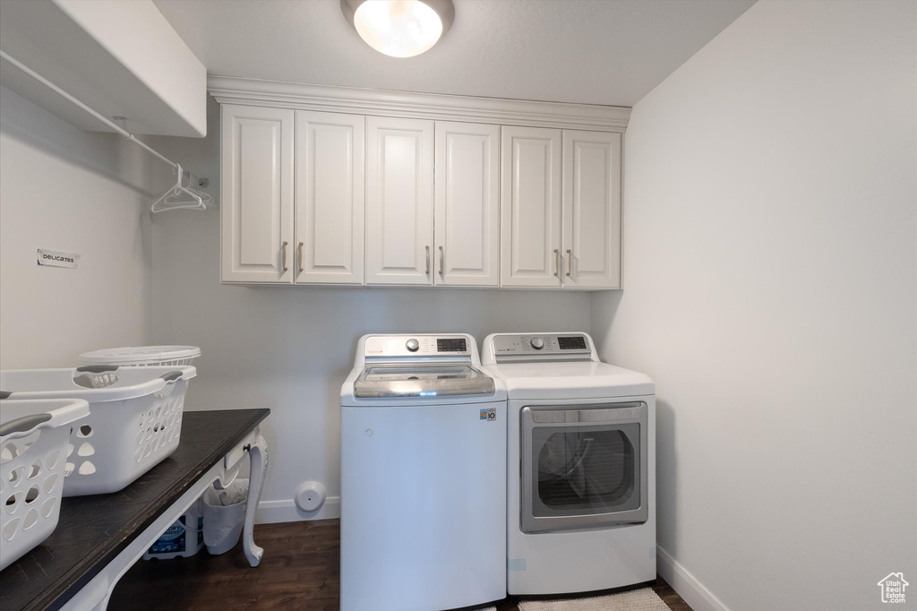 Laundry room with washing machine and clothes dryer, cabinet space, and wood finished floors