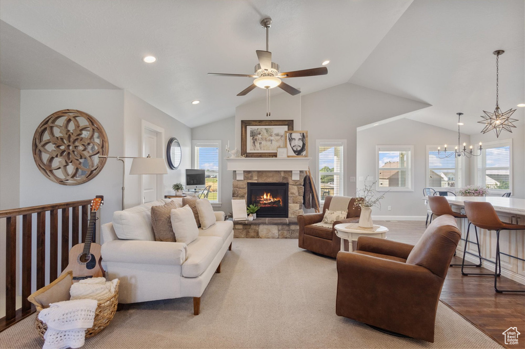 Living room with a chandelier, a ceiling fan, lofted ceiling, a stone fireplace, and wood finished floors