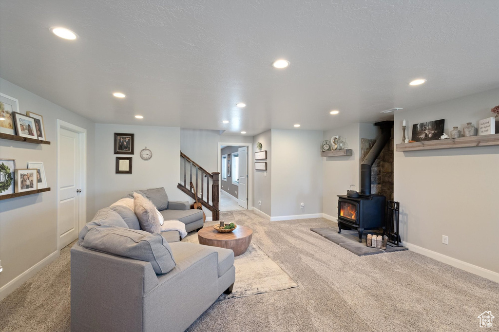 Living area featuring a wood stove, light carpet, recessed lighting, and stairs