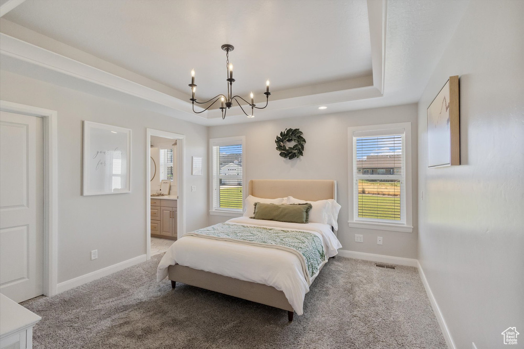 Carpeted bedroom featuring a chandelier, a raised ceiling, multiple windows, and connected bathroom