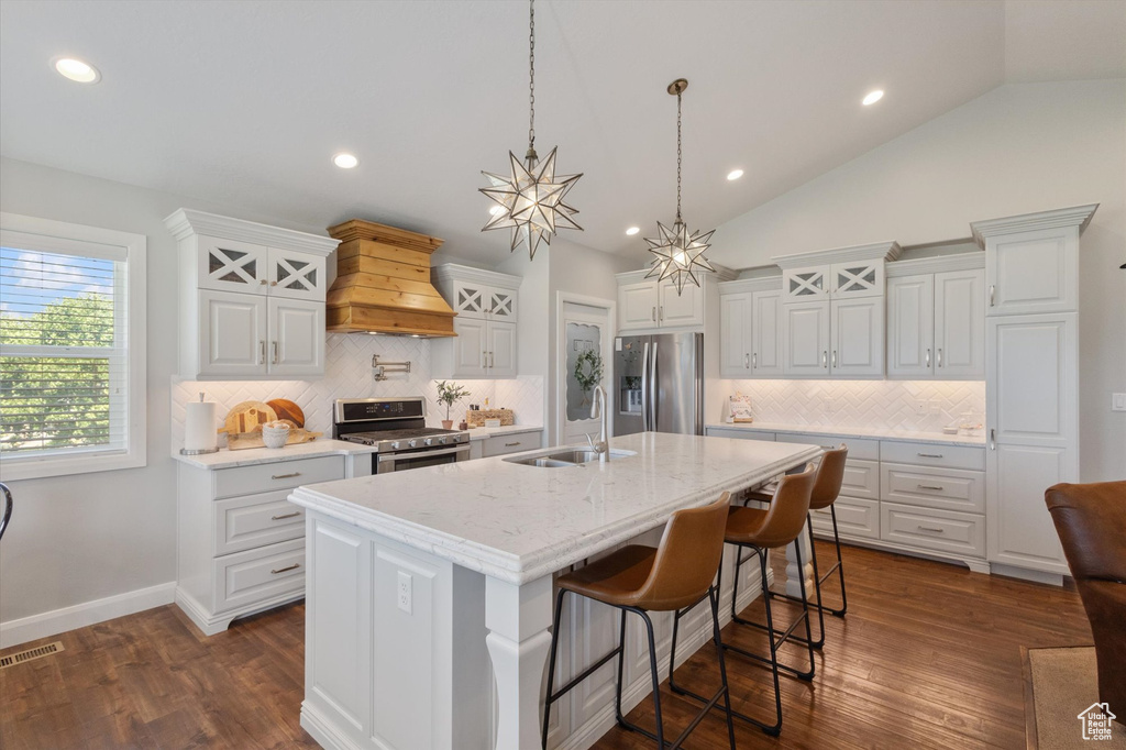 Kitchen featuring appliances with stainless steel finishes, custom exhaust hood, white cabinets, tasteful backsplash, and vaulted ceiling