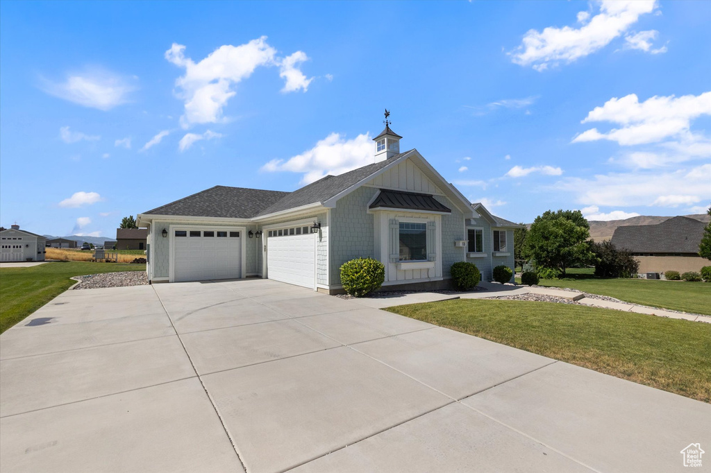Ranch-style home with an attached garage, a front lawn, concrete driveway, a standing seam roof, and board and batten siding