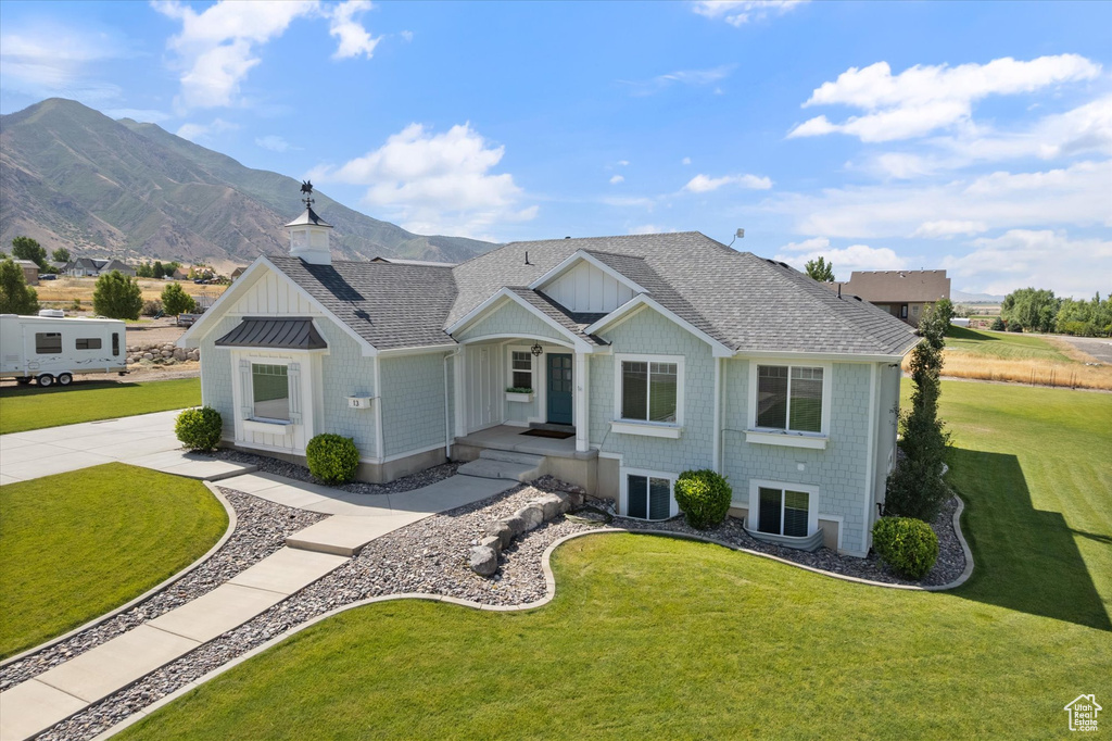 View of front of home with a shingled roof, a front yard, a mountain view, and board and batten siding