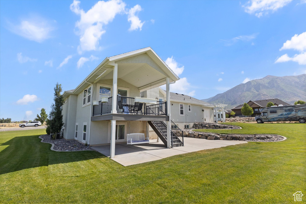Back of house featuring a patio, a mountain view, stucco siding, stairway, and a lawn