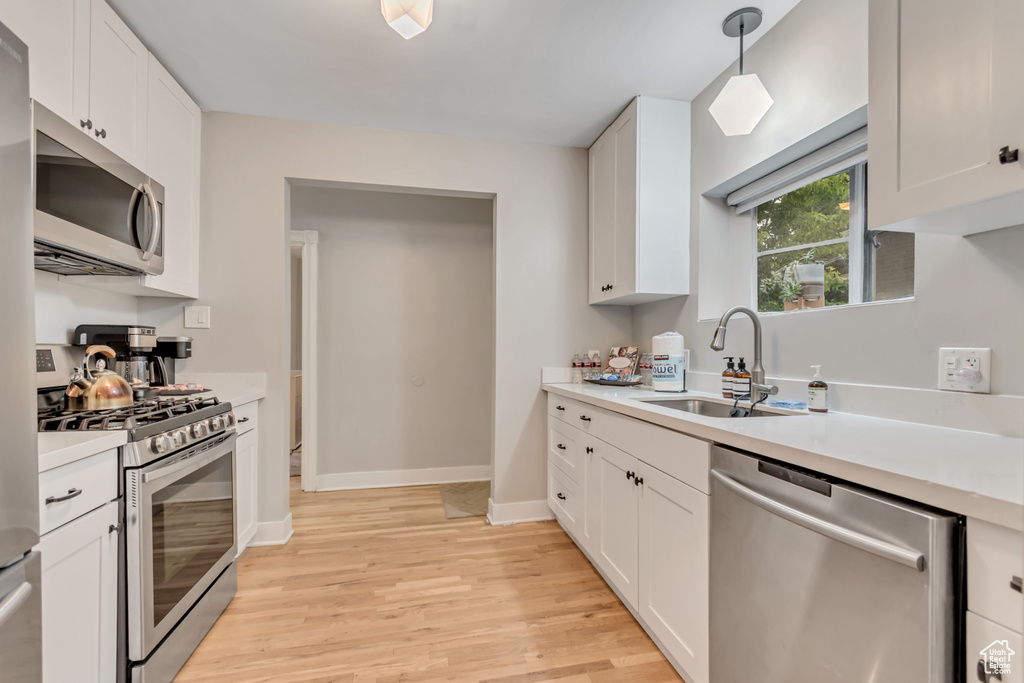 Kitchen with appliances with stainless steel finishes, light wood-style floors, light countertops, white cabinetry, and hanging light fixtures