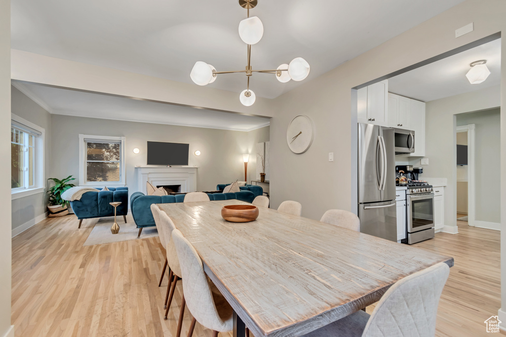 Dining room featuring light wood-style flooring, a chandelier, a fireplace, and crown molding