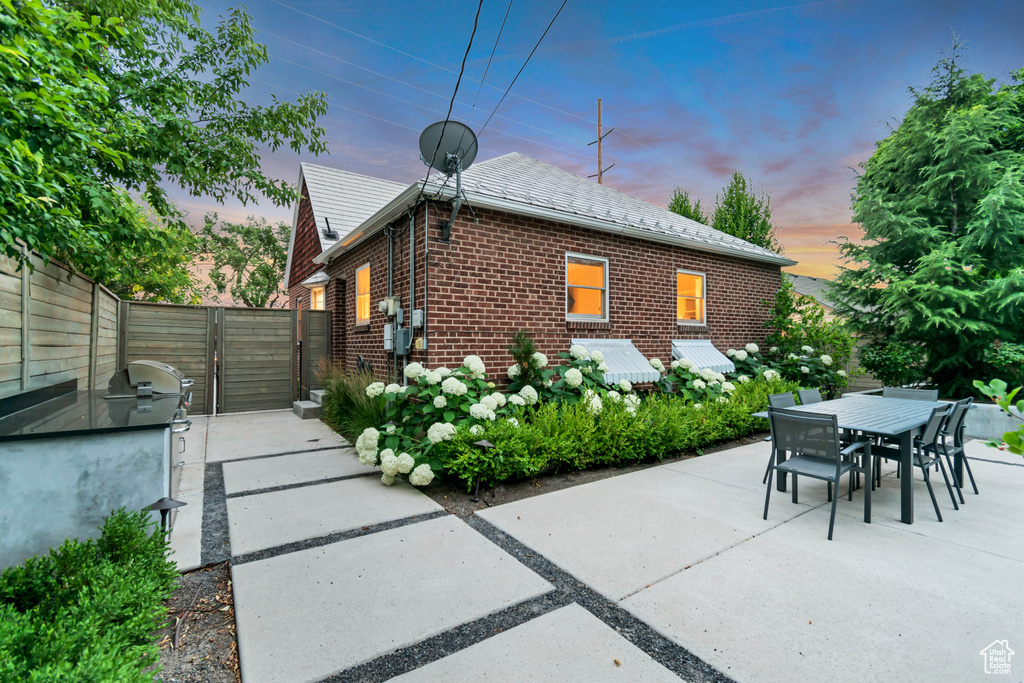 Back of house at dusk with brick siding, a gate, outdoor dining area, and a patio area