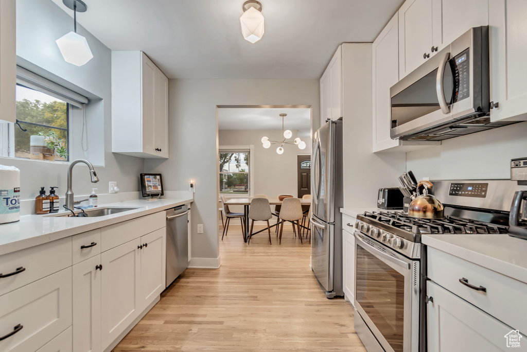 Kitchen with stainless steel appliances, light wood-style flooring, white cabinetry, light countertops, and hanging light fixtures