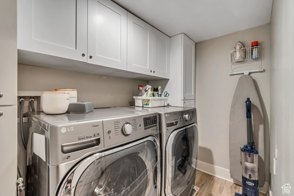 Laundry room featuring washer and clothes dryer, cabinet space, and light wood-type flooring