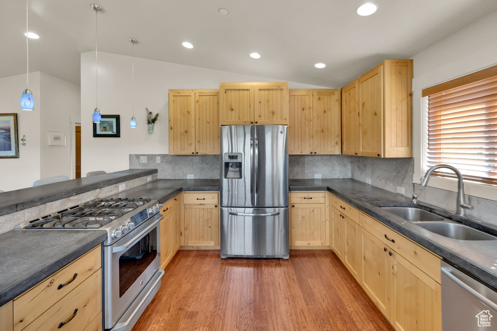 Kitchen with stainless steel appliances, light brown cabinets, vaulted ceiling, dark countertops, and light wood finished floors