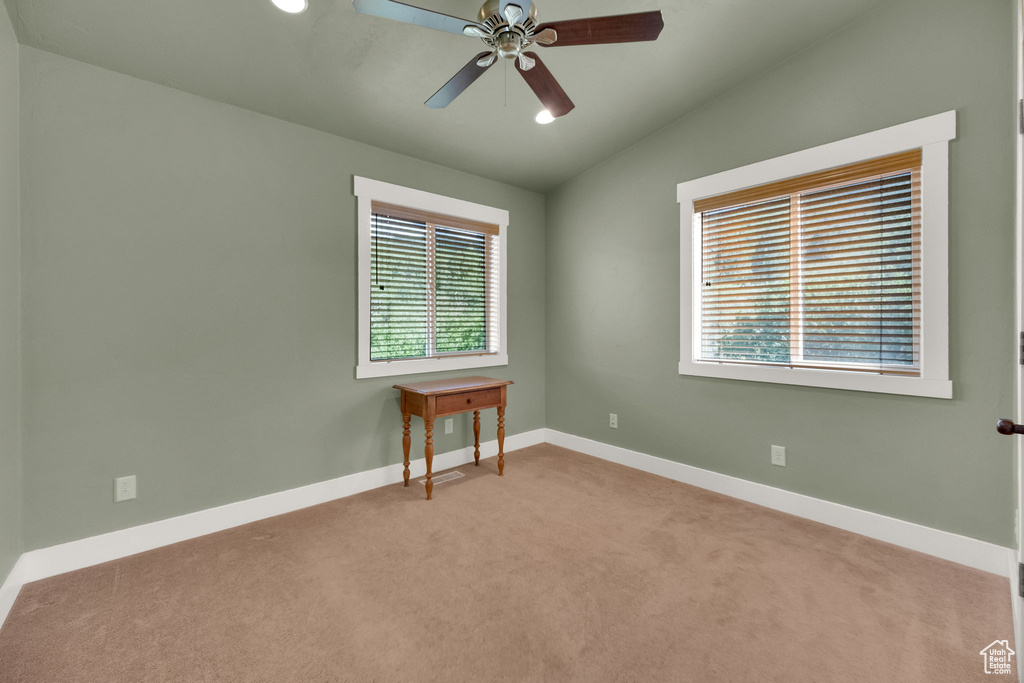 Empty room with light carpet, plenty of natural light, lofted ceiling, and a ceiling fan