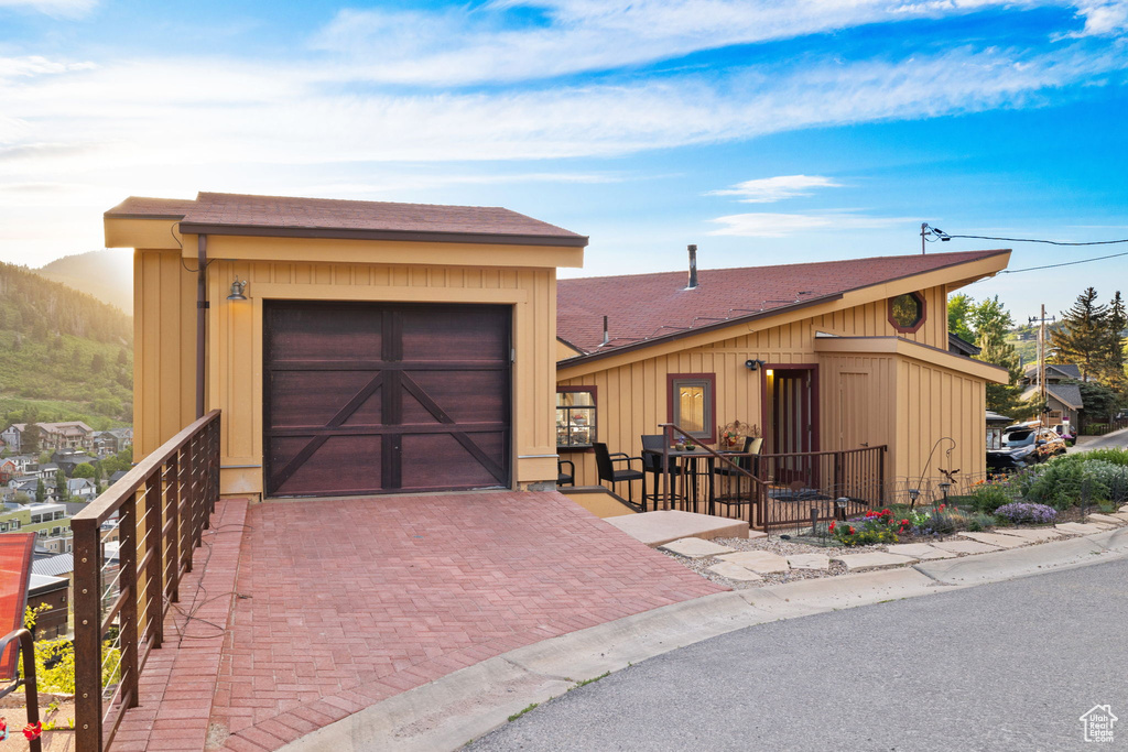 View of front of home featuring an attached garage, a shingled roof, and decorative driveway