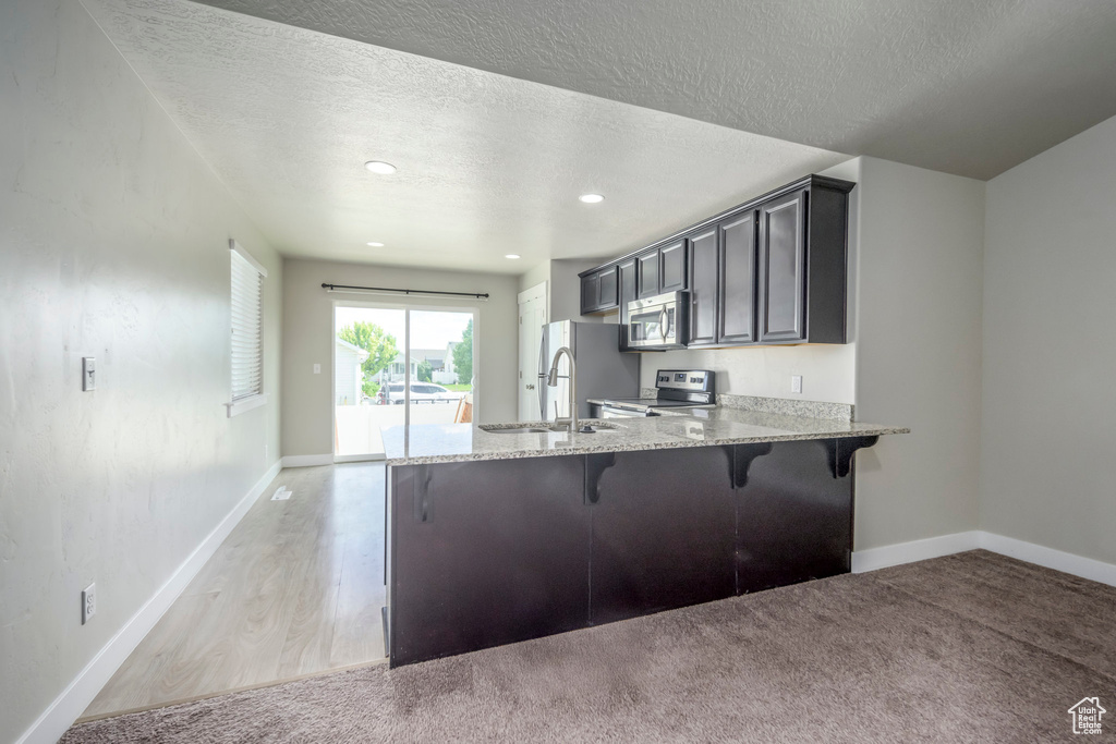 Kitchen with appliances with stainless steel finishes, a kitchen bar, light stone countertops, a peninsula, and a textured ceiling