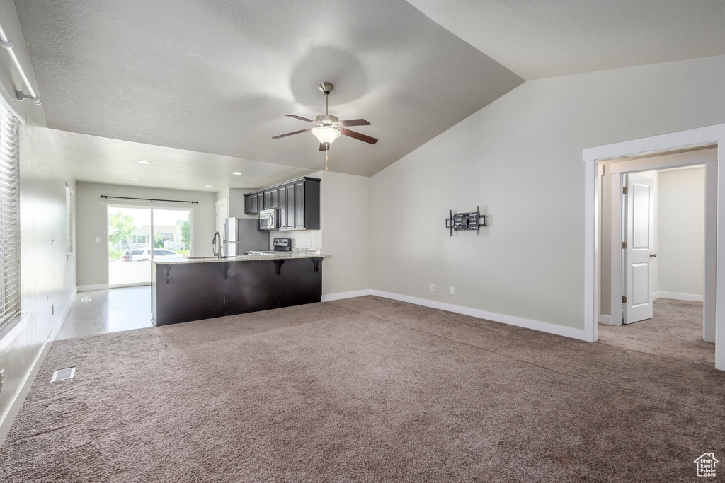 Unfurnished living room with ceiling fan, vaulted ceiling, and light colored carpet