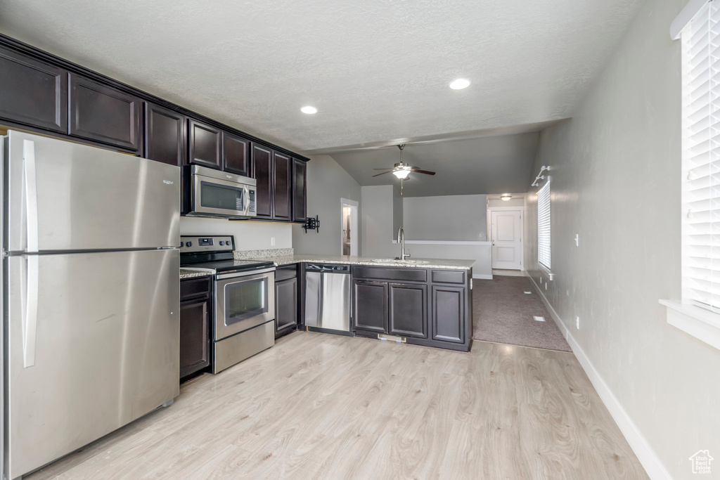 Kitchen with stainless steel appliances, a peninsula, light wood-style flooring, ceiling fan, and vaulted ceiling