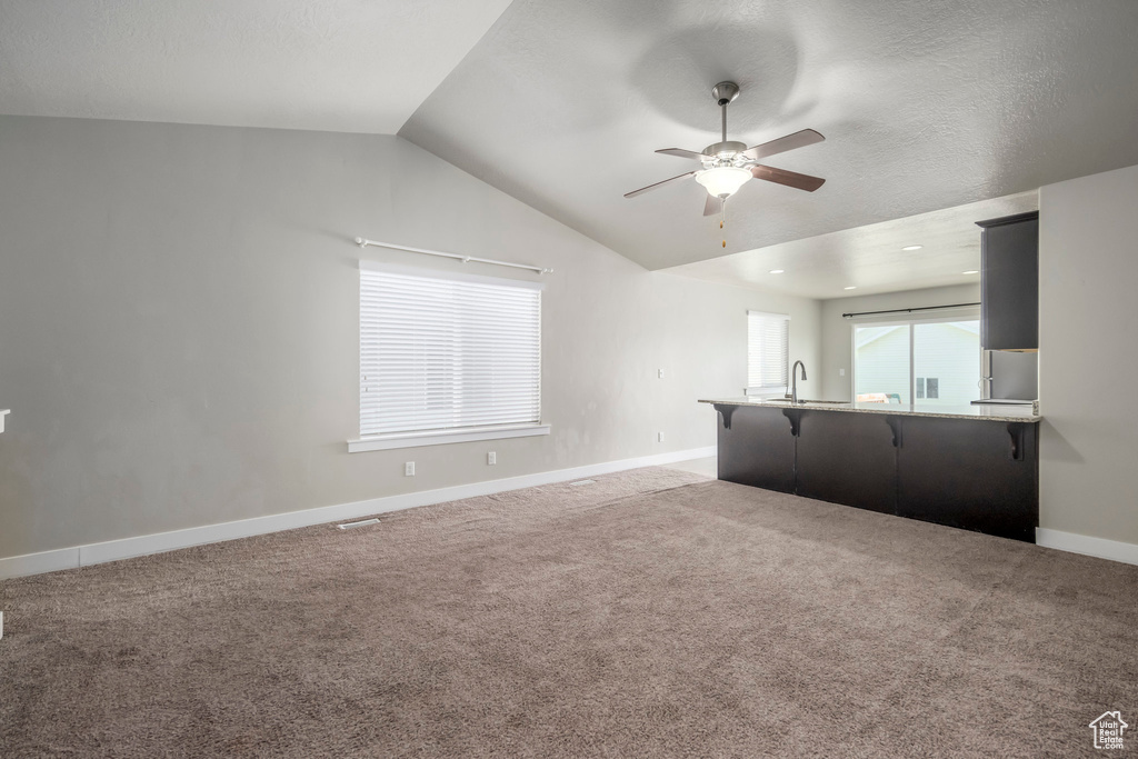Unfurnished living room with a ceiling fan, lofted ceiling, and carpet flooring