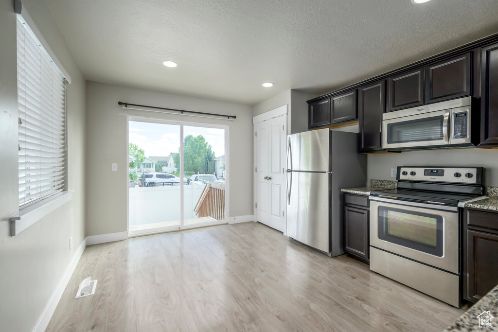 Kitchen featuring stainless steel appliances, light wood-style flooring, recessed lighting, light stone counters, and a textured ceiling