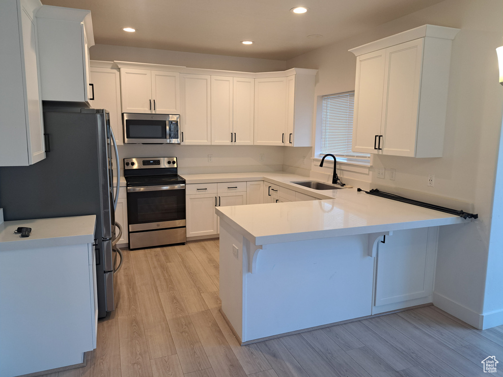Kitchen with stainless steel appliances, a peninsula, light wood finished floors, white cabinets, and recessed lighting