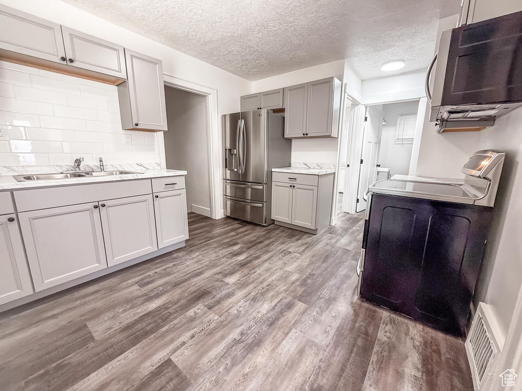 Kitchen with appliances with stainless steel finishes, gray cabinetry, wood finished floors, a textured ceiling, and light countertops