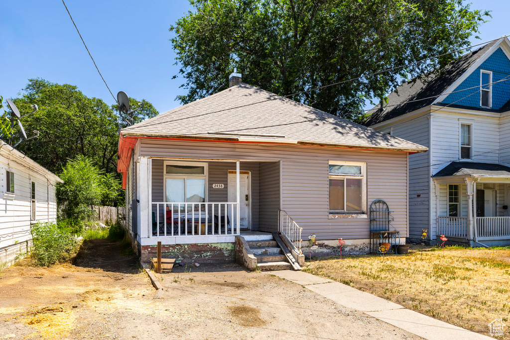 View of front of property featuring covered porch, a chimney, and roof with shingles