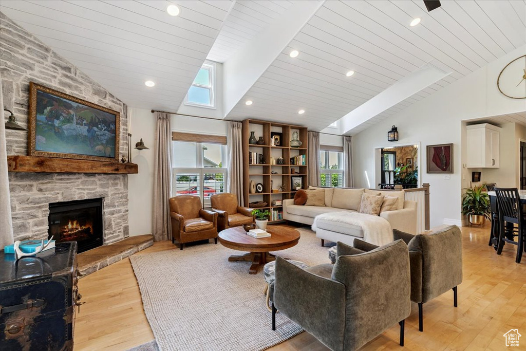 Living room featuring vaulted ceiling, light wood finished floors, plenty of natural light, a fireplace, and wooden ceiling