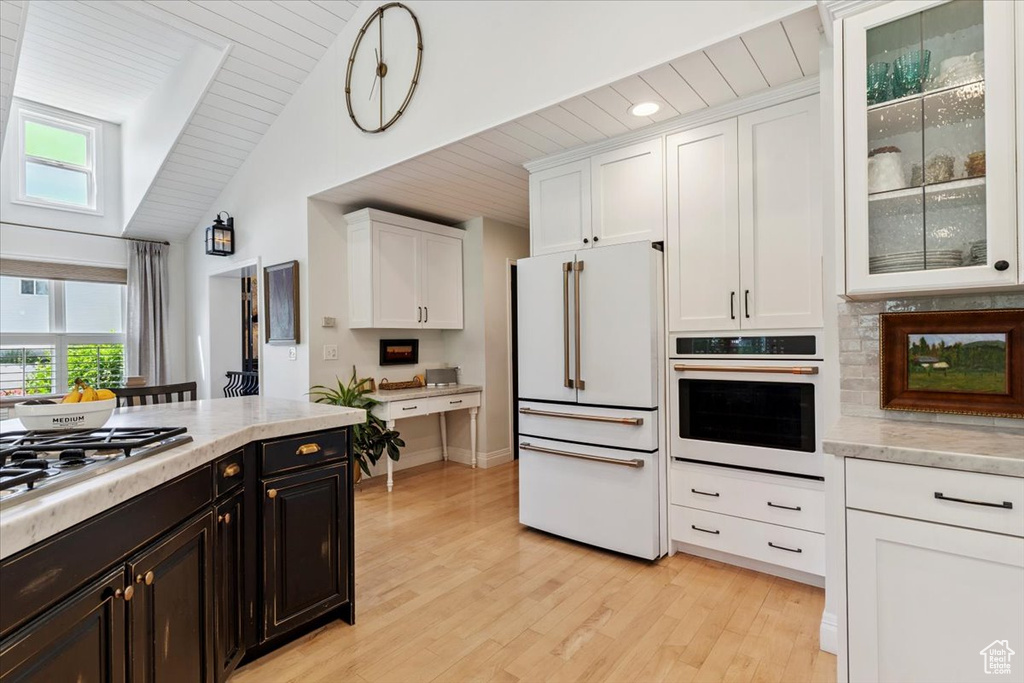 Kitchen featuring white appliances, white cabinets, plenty of natural light, light wood-type flooring, and vaulted ceiling