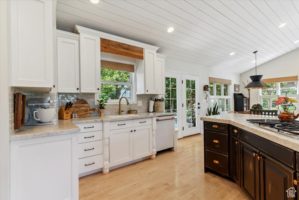 Kitchen featuring white dishwasher, stainless steel gas stovetop, white cabinetry, light wood-style floors, and decorative backsplash