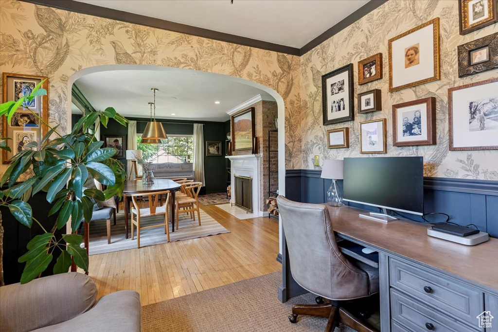 Office featuring wallpapered walls, arched walkways, wainscoting, crown molding, and light wood-style floors