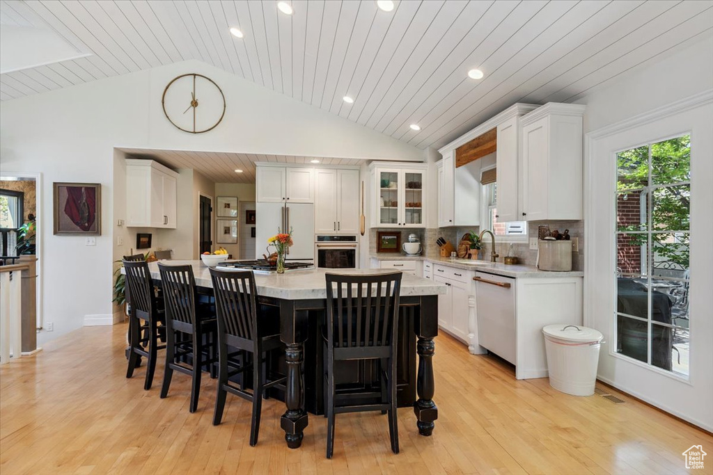 Kitchen with stainless steel dishwasher, lofted ceiling, white cabinets, a kitchen bar, and a kitchen island