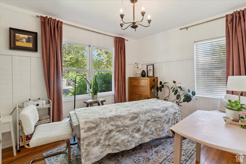 Bedroom featuring a decorative wall, multiple windows, a chandelier, wood finished floors, and a wainscoted wall