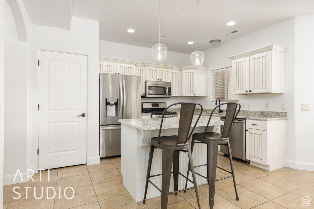 Kitchen featuring stainless steel appliances, light tile patterned floors, a breakfast bar, light stone countertops, and recessed lighting