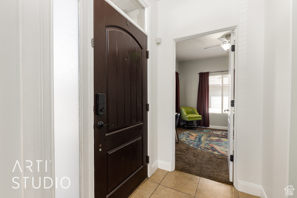 Entrance foyer with light tile patterned floors, light colored carpet, and a ceiling fan