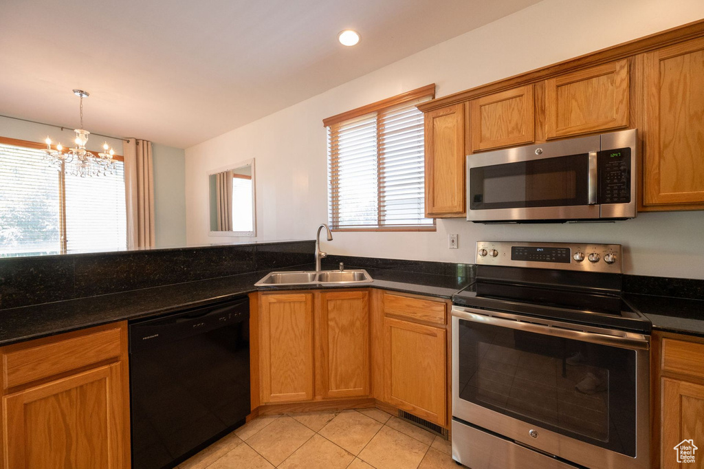 Kitchen with appliances with stainless steel finishes, a chandelier, light tile patterned floors, brown cabinets, and recessed lighting