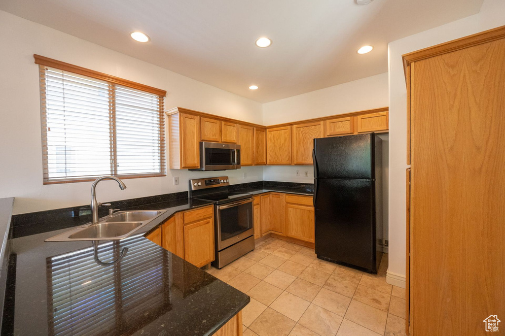 Kitchen featuring stainless steel appliances, recessed lighting, light tile patterned floors, dark stone countertops, and brown cabinetry