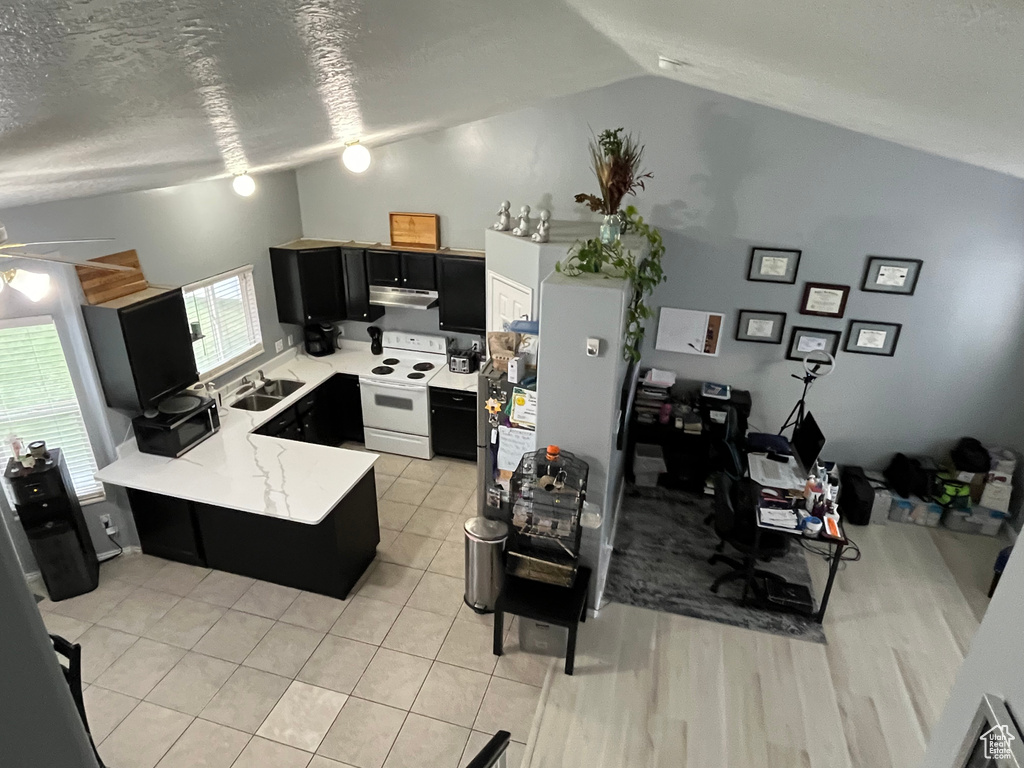 Kitchen featuring white range with electric stovetop, dark cabinetry, lofted ceiling, a peninsula, and under cabinet range hood