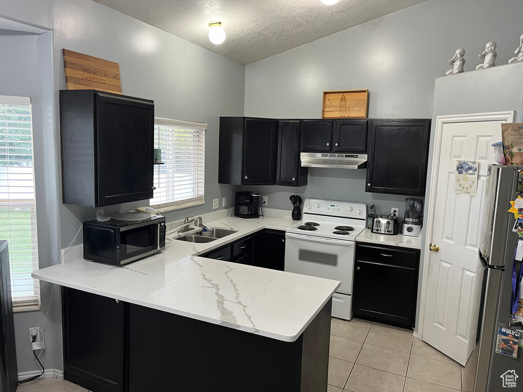 Kitchen with white range with electric stovetop, under cabinet range hood, dark cabinetry, freestanding refrigerator, and a peninsula