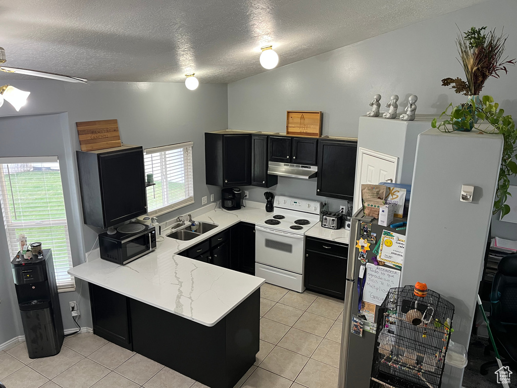Kitchen featuring under cabinet range hood, white electric stove, dark cabinetry, a peninsula, and a textured ceiling