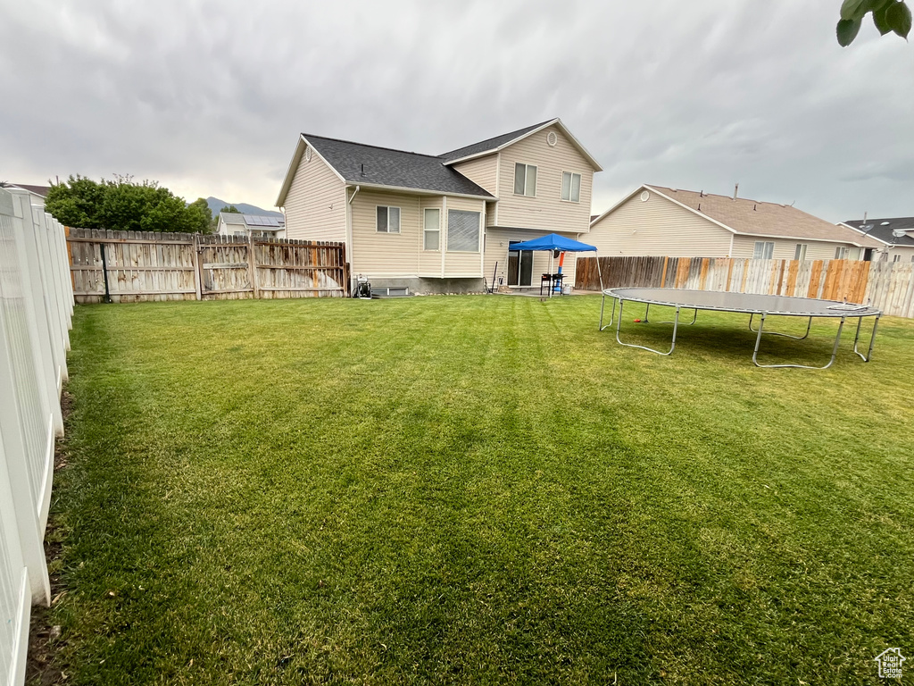 Back of house with a trampoline and a fenced backyard